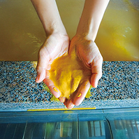 汐湯温泉の黄色い温泉沈殿抽出物を両手ですくう画像。